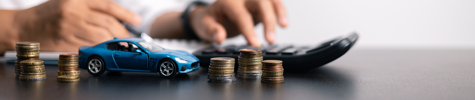 Man achter bureau met een pen, rekenmachine, miniatuur auto en stapels muntgeld